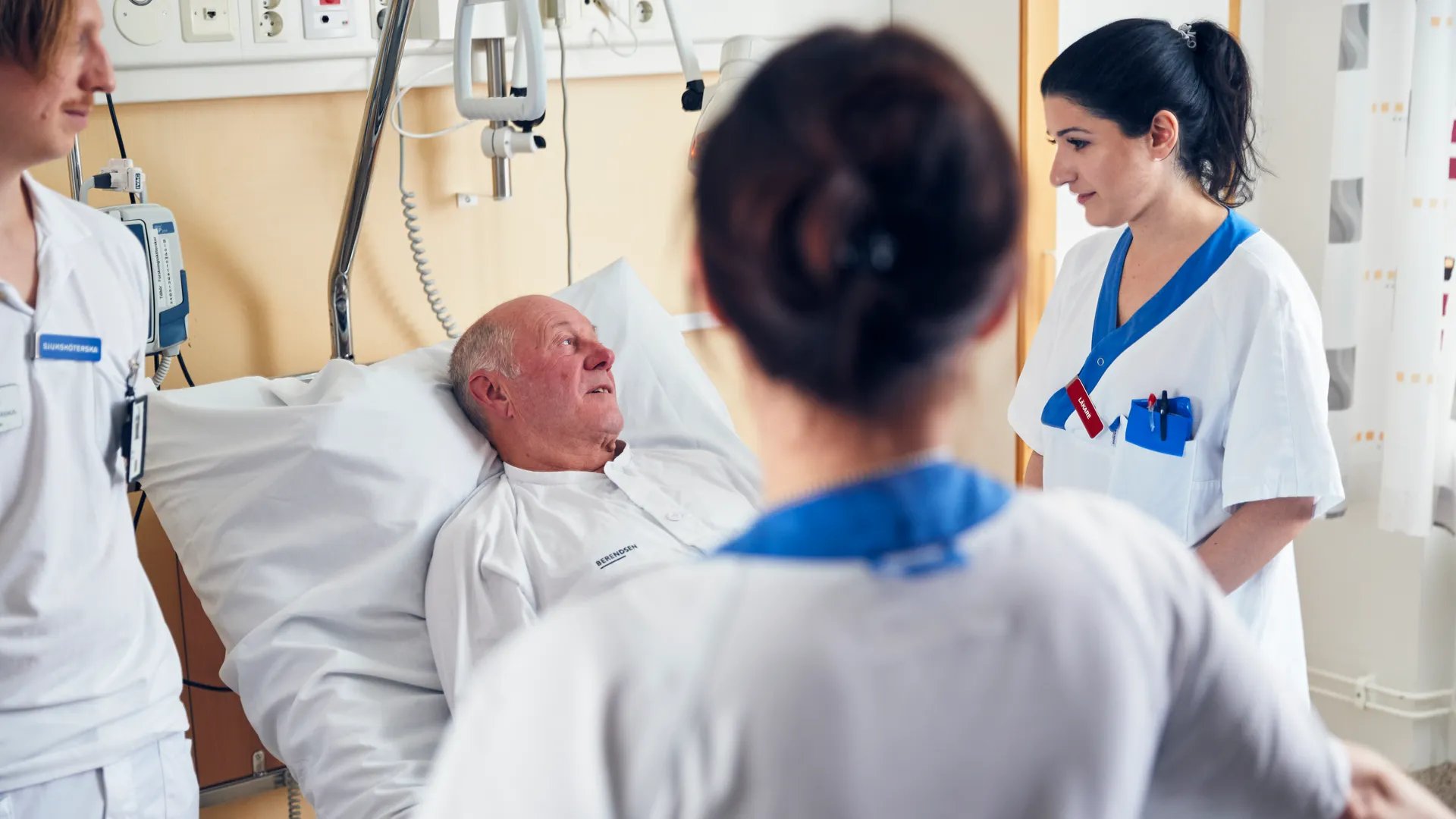 En sjuksköterska pratar med en patient i en sjukhussäng.